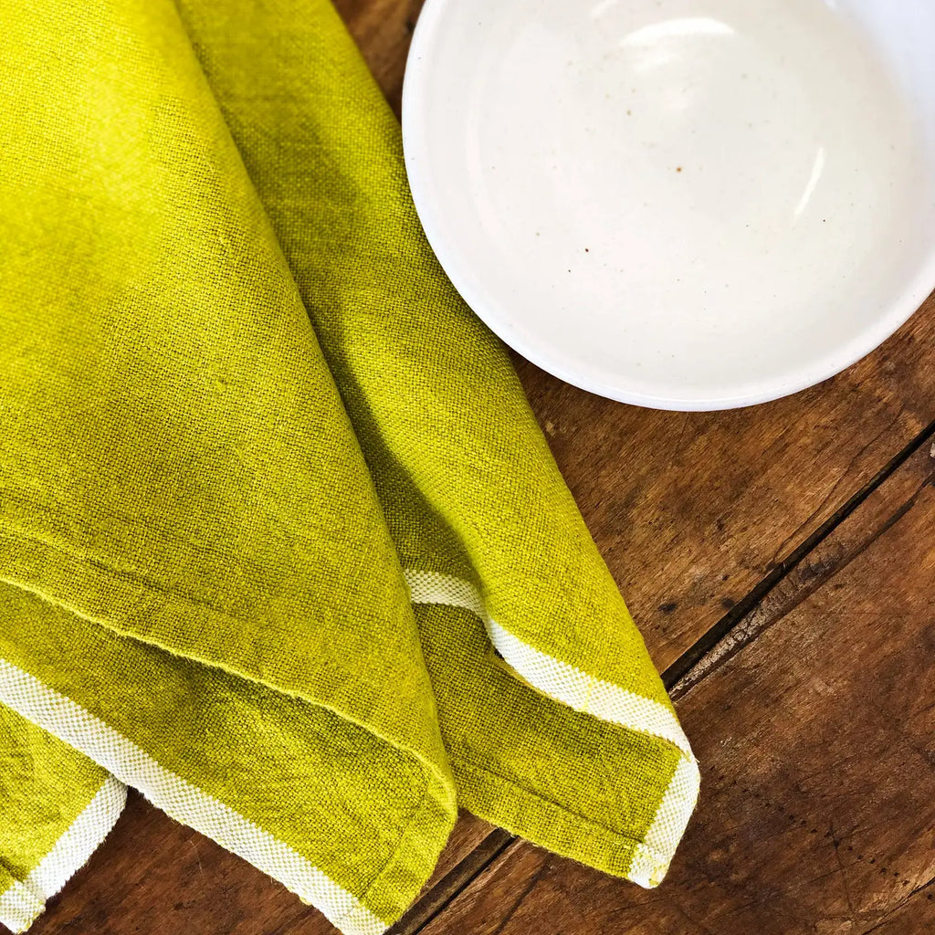 Green towel with white trim on a wooden surface next to a white plate