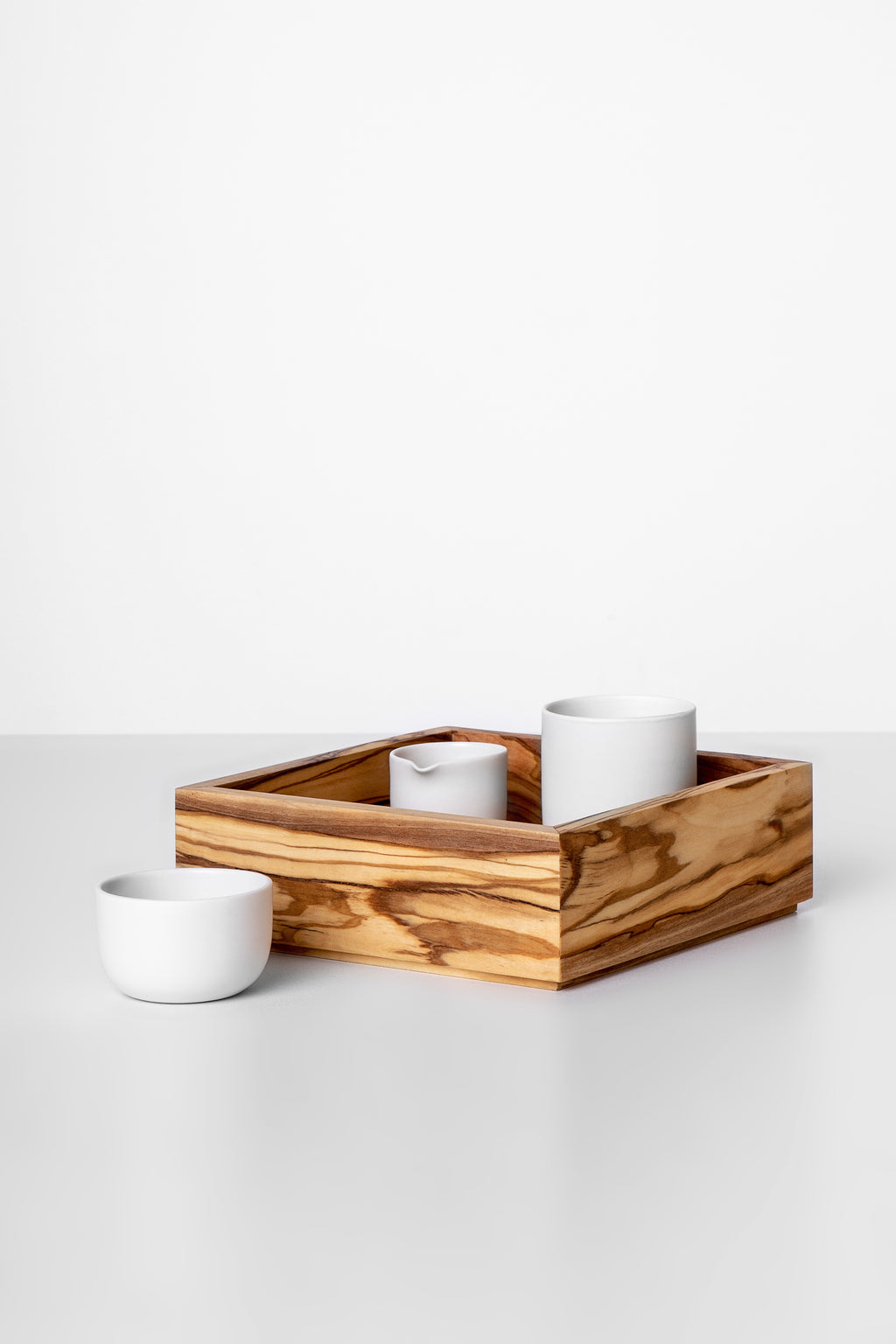 A rectangular olive wood serving tray with three compartments, featuring a natural grain pattern, used to present two white cups.