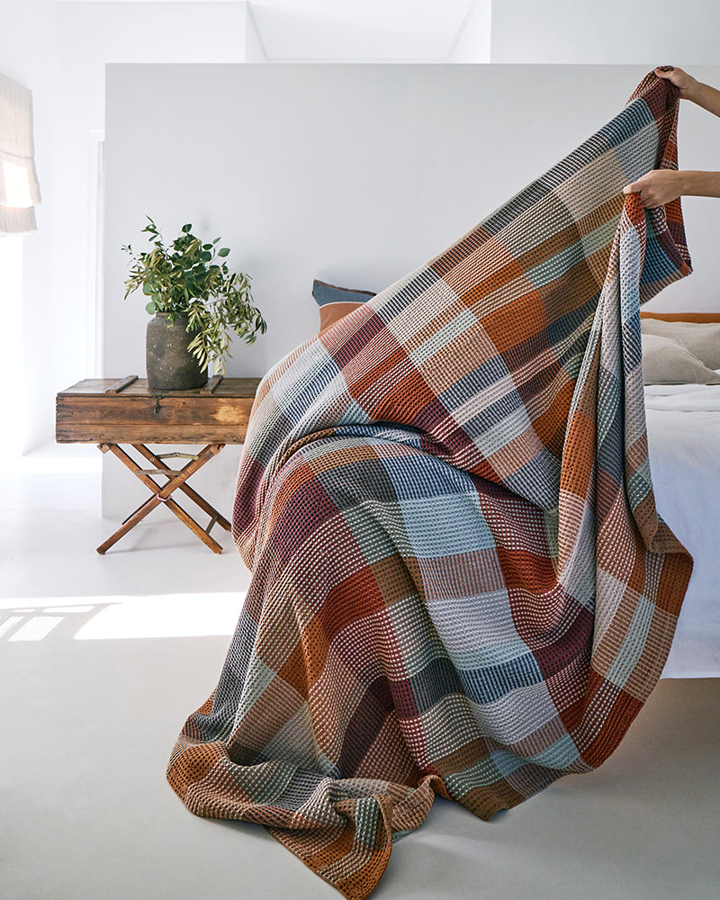Person putting 100% cotton blanket on bed.