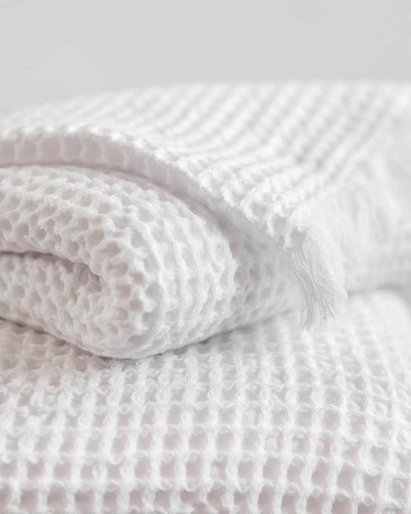 A folded white organic cotton Belgian waffle bath towel displaying its textured waffle weave pattern.