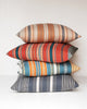 A variety of pillows with different patterns and colors stacked on top of each other with a white background.