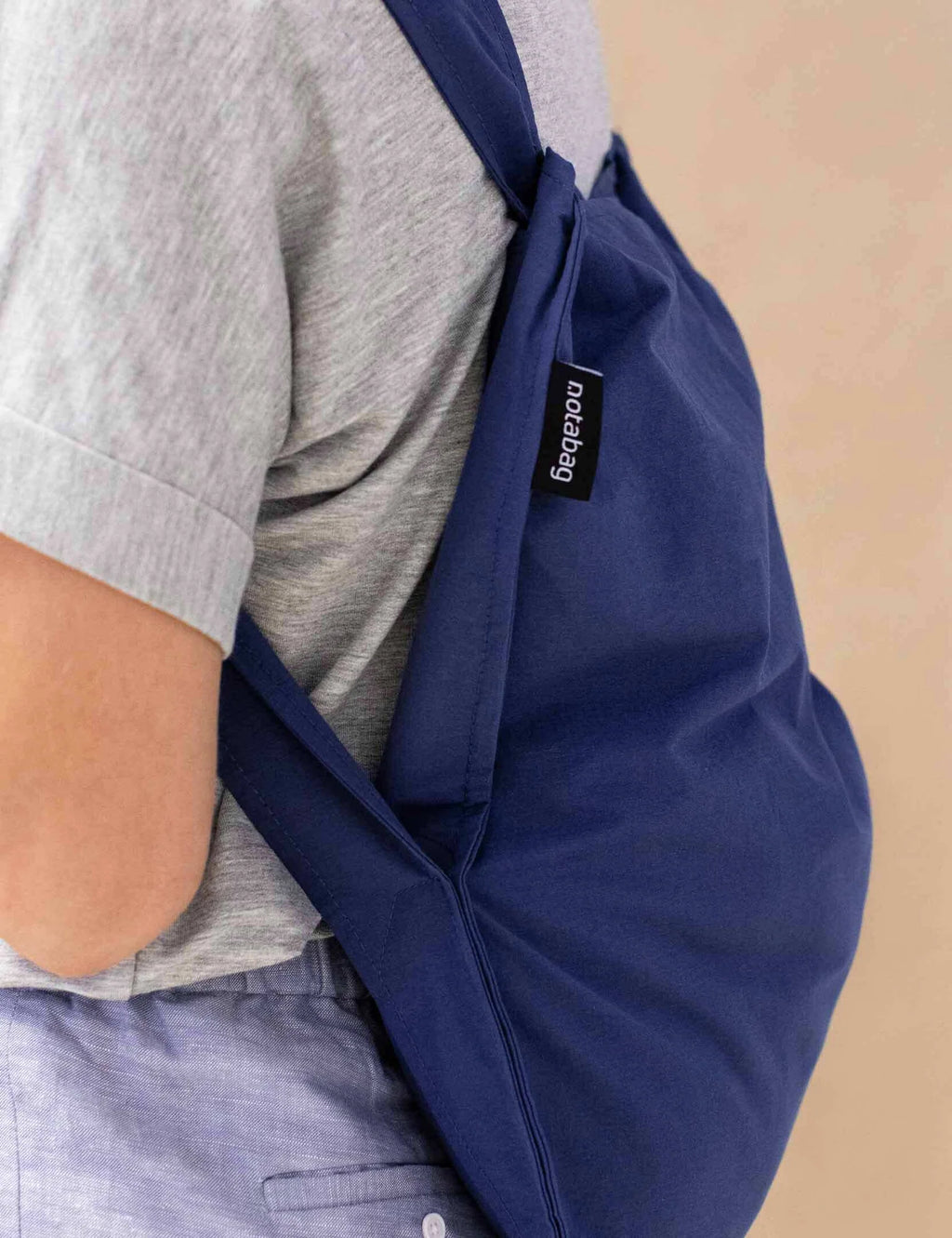 Person wearing a navy sling bag with a brand label on a beige background