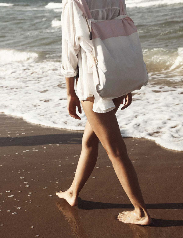 Person walking on a beach with a colorful bag