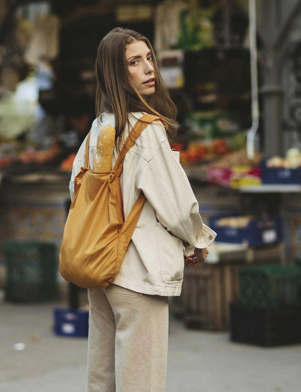Woman with a yellow backpack standing in an outdoor market setting