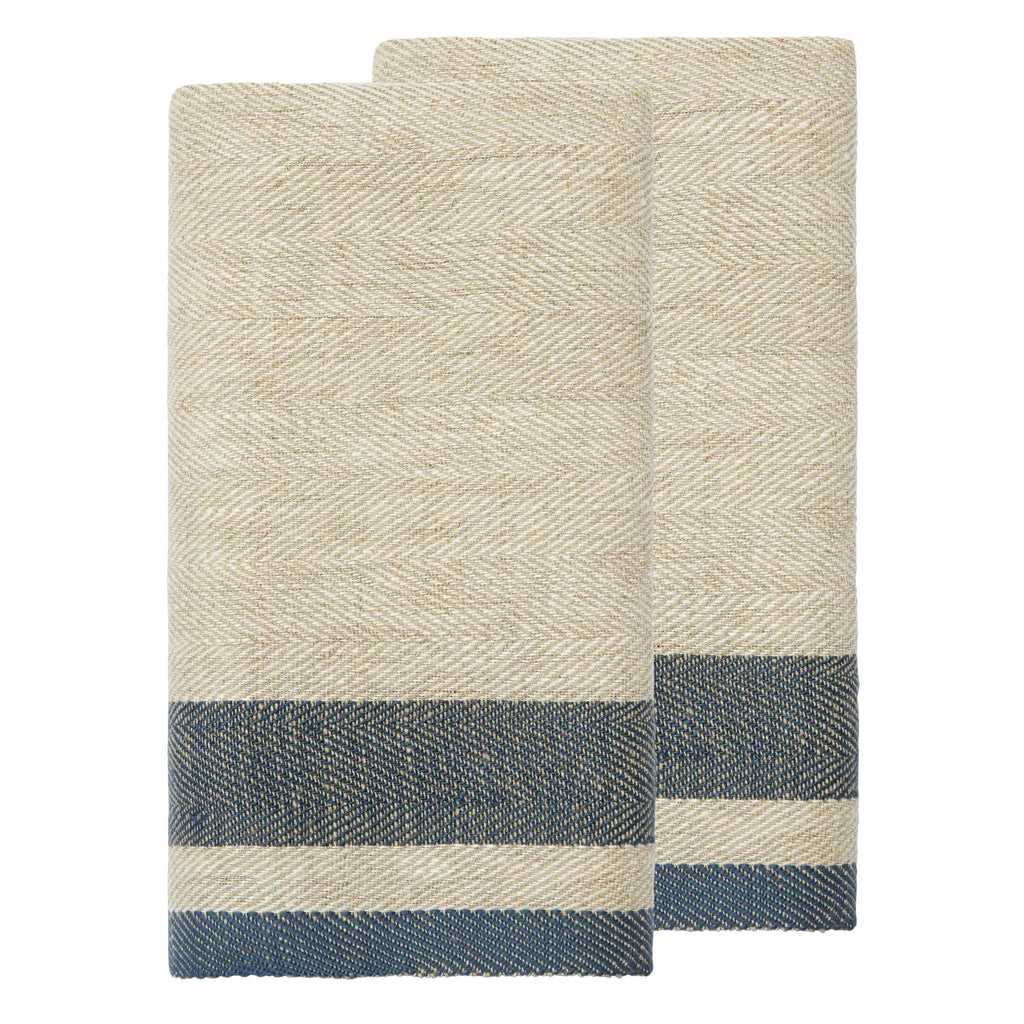 Two folded woven towels in a natural beige color with a herringbone pattern and a navy blue striped border near the bottom, shown on a plain white background.