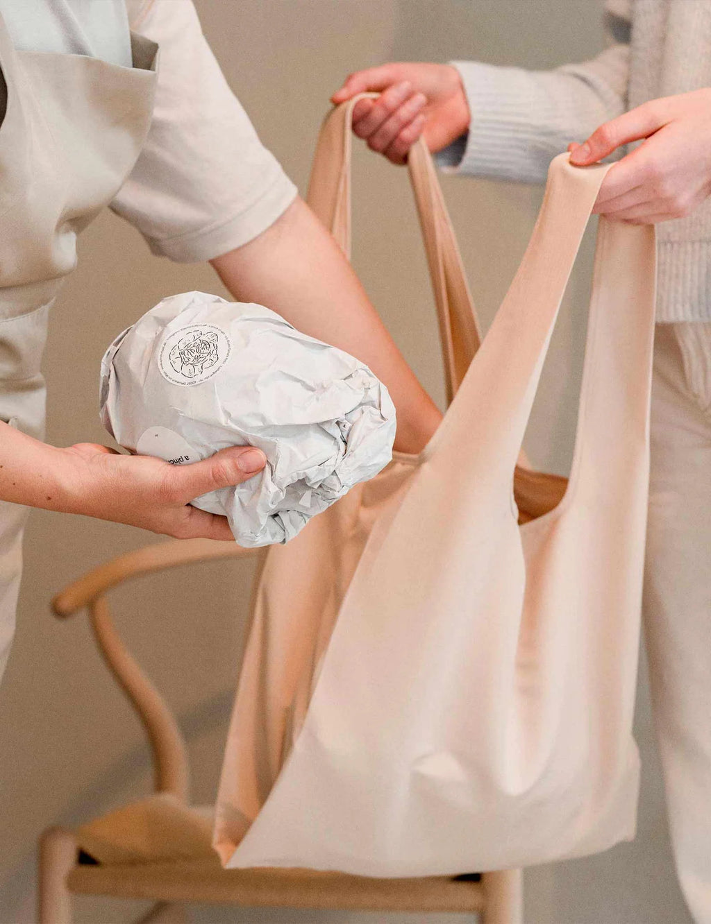 Two people holding a beige tote bag with a chair in the background