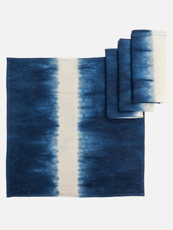 A set of blue and white hand-dyed cotton table linens including a tablecloth and napkins displayed on a white background.