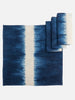 A set of blue and white hand-dyed cotton table linens including a tablecloth and napkins displayed on a white background.