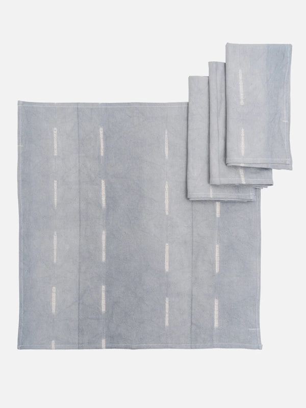 A collection of blue and white hand-dyed cotton table linens, including a tablecloth and napkins, displayed on a white background.