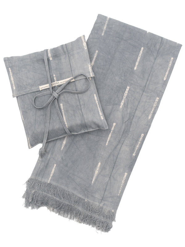 A gray cotton throw blanket with fringes and a matching pouch, displayed neatly folded.