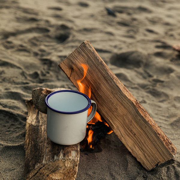 Camping scene with a mug on a small fire built into the sand.