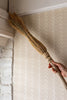 Hand holding a broom against a wall with a herringbone pattern