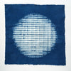 A square indigo blue fabric square with a white tie-dye shibori circle in the center, displayed flat against a white background.