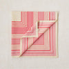 A folded scarf with a geometric stripe pattern in rose pink, cherry red, and clotted cream colors, displaying the Lorna Murray brand name.