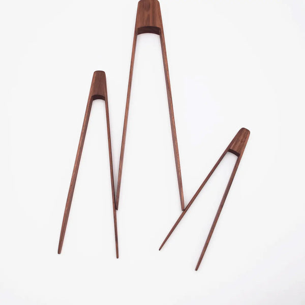A set of walnut wood tongs in three different sizes placed on a white surface.