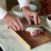 Person cutting meat on a wooden cutting board with a white plate in the background