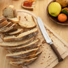 Sliced bread on a wooden cutting board with a knife, surrounded by fruits.