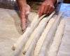 Hands shaping dough into long, thin loaves on a cloth surface.