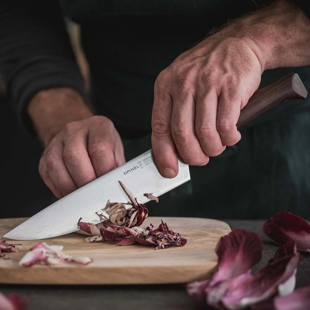 Person cutting red onions on a wooden board with a chef's knife.