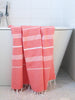 Coral towel with white stripes draped over a white bathtub in a bathroom setting.