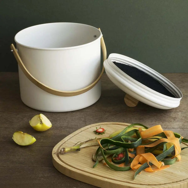 White compostable bin with a wooden lid on a dark surface with food waste.