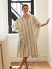 Woman wearing a striped kaftan standing in a room with a window.