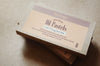A box of Smilogy Beeswax Oil Pastels resting on a neutral beige surface. The packaging features a soft beige label with a dusty purple top band and dark brown text, with another box partially visible underneath.