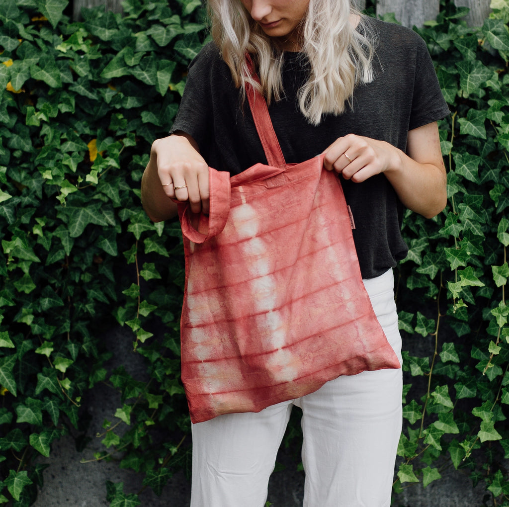 Person holding a tie-dye tote bag in front of a green ivy wall