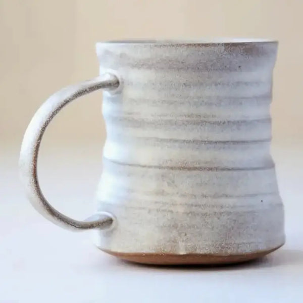 A handmade ceramic mug with a textured, ribbed surface and a curved handle, shown against a neutral beige background.
