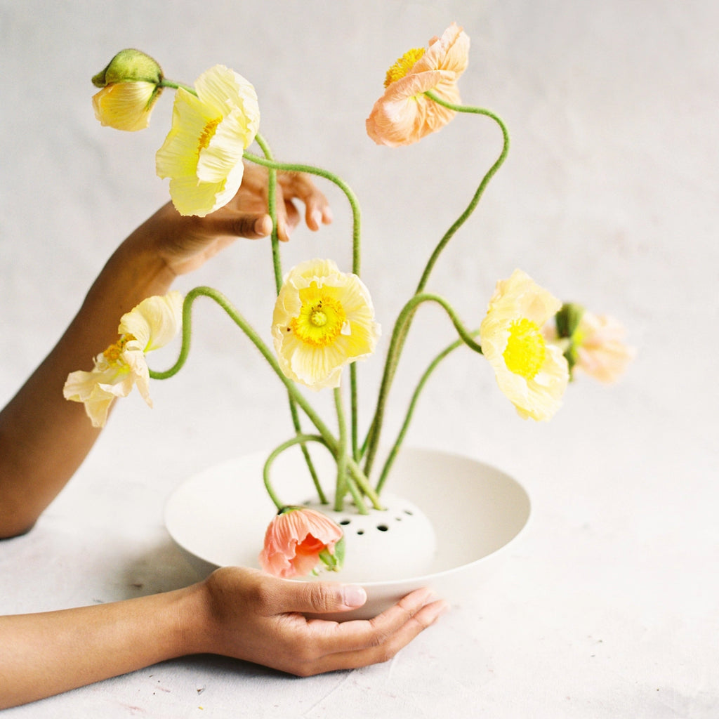 Person holding a white vase with yellow flowers on a light background