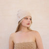 Woman wearing a beige knit beanie and strapless top against a light pink background