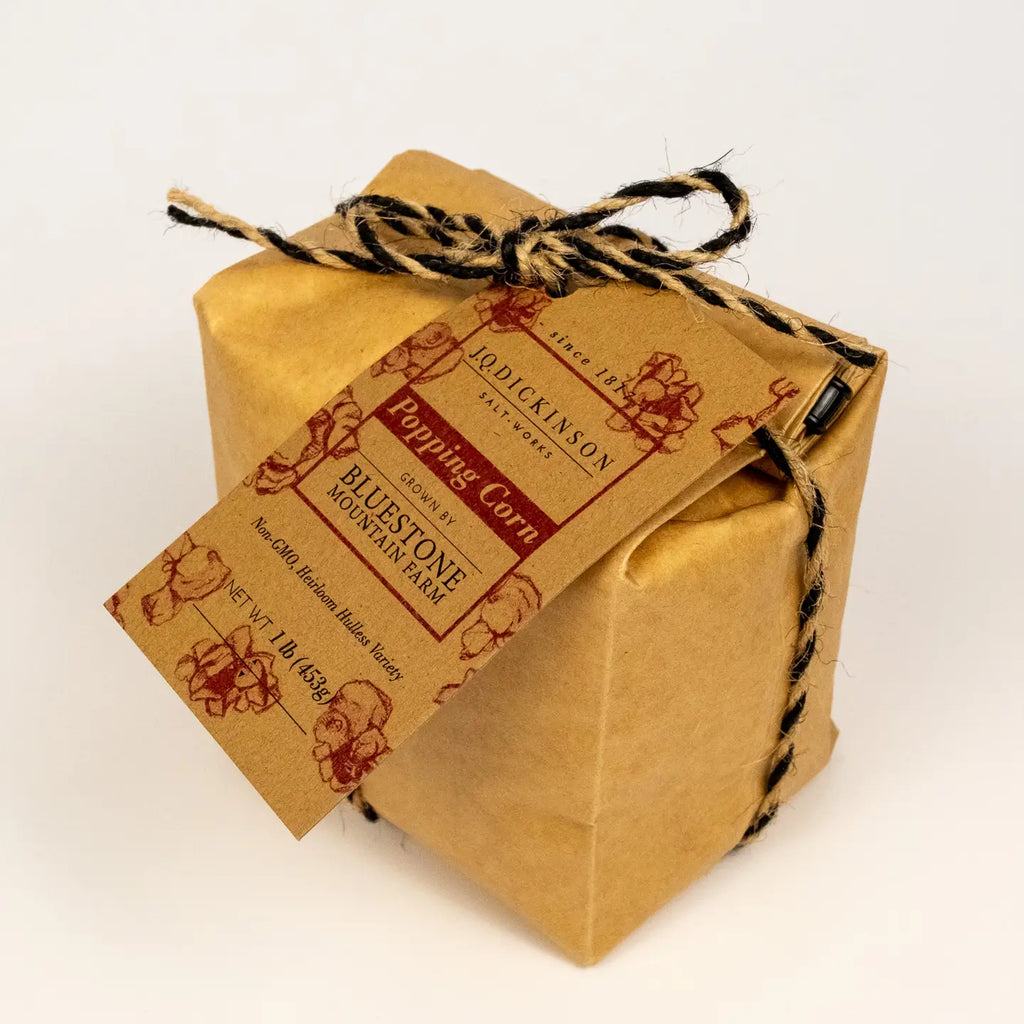 A square kraft paper gift box wrapped with black-and-brown twine and a printed paper tag reading 'Popping Corn Bluestone Mountain Farm,' photographed on a clean white background.