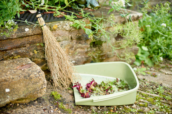 Garden scene with a broom and compost bin filled with garden waste.
