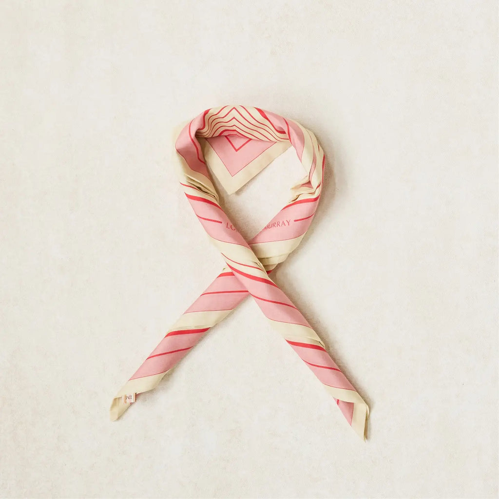 A looped scarf with a geometric stripe pattern in rose pink, cherry red, and clotted cream colors.