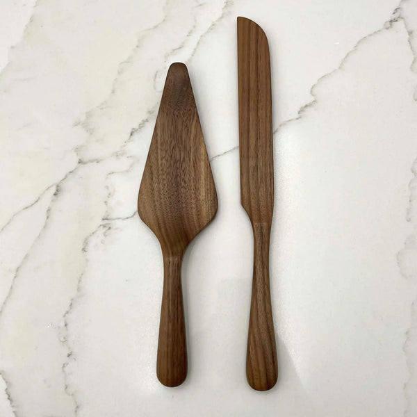 A set of two walnut wood cake serving tools, one knife and one server, placed on a marble surface.