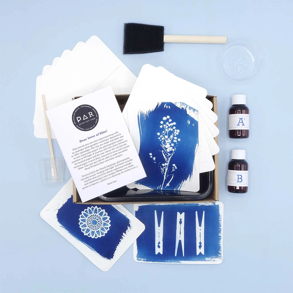 A flat-lay view of a D&H Blue Silk Screen kit on a light blue background, containing silk screen templates, two bottles of dye solution, a foam brush, and instruction cards.