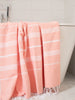 Pink towel with white stripes draped over a bathtub in a bathroom setting.