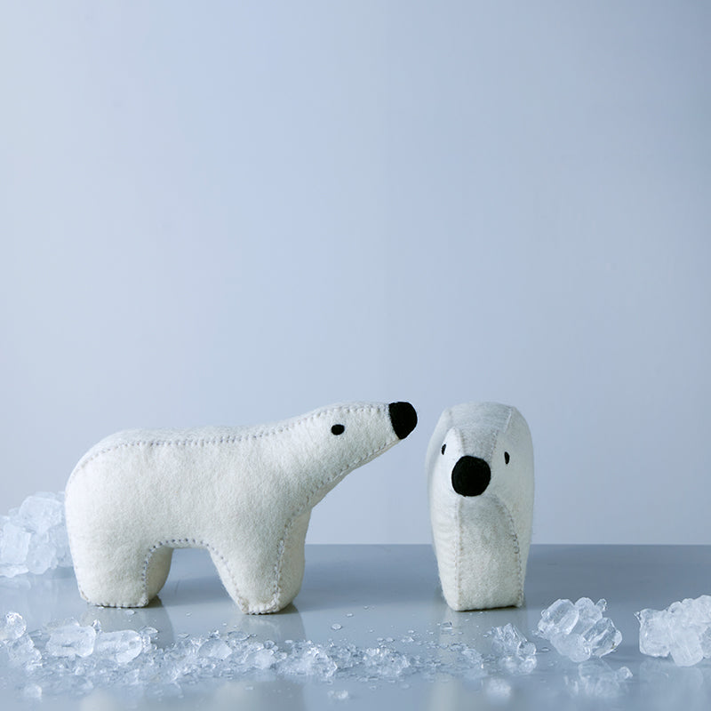 Two stuffed bears, one larger and one smaller, made of wool, appearing to interact with the larger one, which is on a shelf with ice cubes around it.