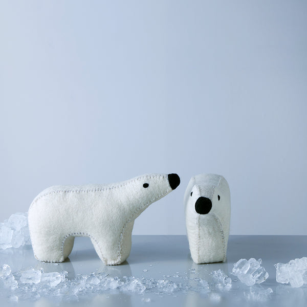 Two stuffed bears, one larger and one smaller, made of wool, appearing to interact with the larger one, which is on a shelf with ice cubes around it.