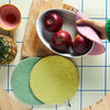 Bowl of apples on a cutting board with colorful pot holders.
