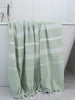 Green towel with white stripes draped over a bathtub in a bathroom setting.