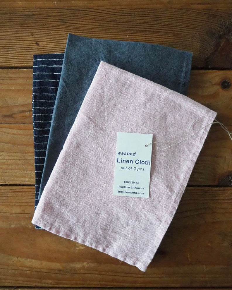 Set of washed linen cloths on a wooden surface with a label indicating the product details.