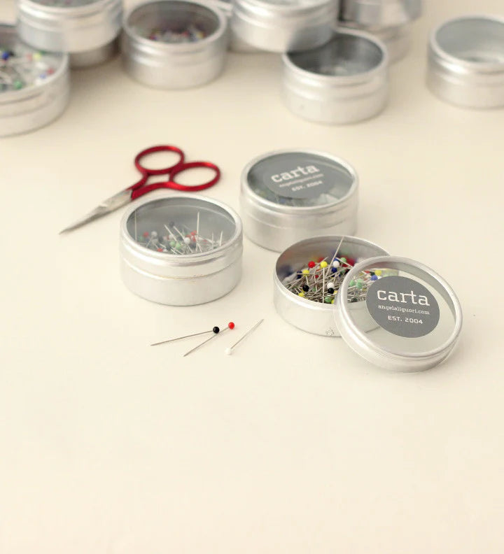 Silver tins with pins and a red scissors on a light background
