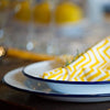 Yellow and white zigzag-patterned napkin on a white plate with blue rim, blurred background