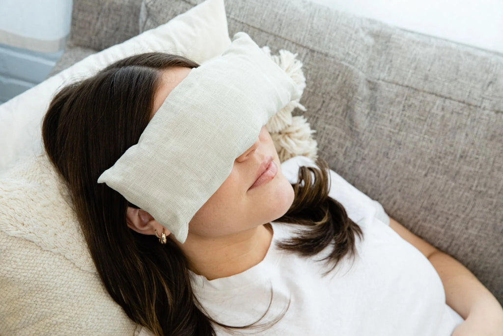 Woman wearing a white eye mask and sitting on a couch.