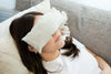 Woman wearing a white eye mask and sitting on a couch.