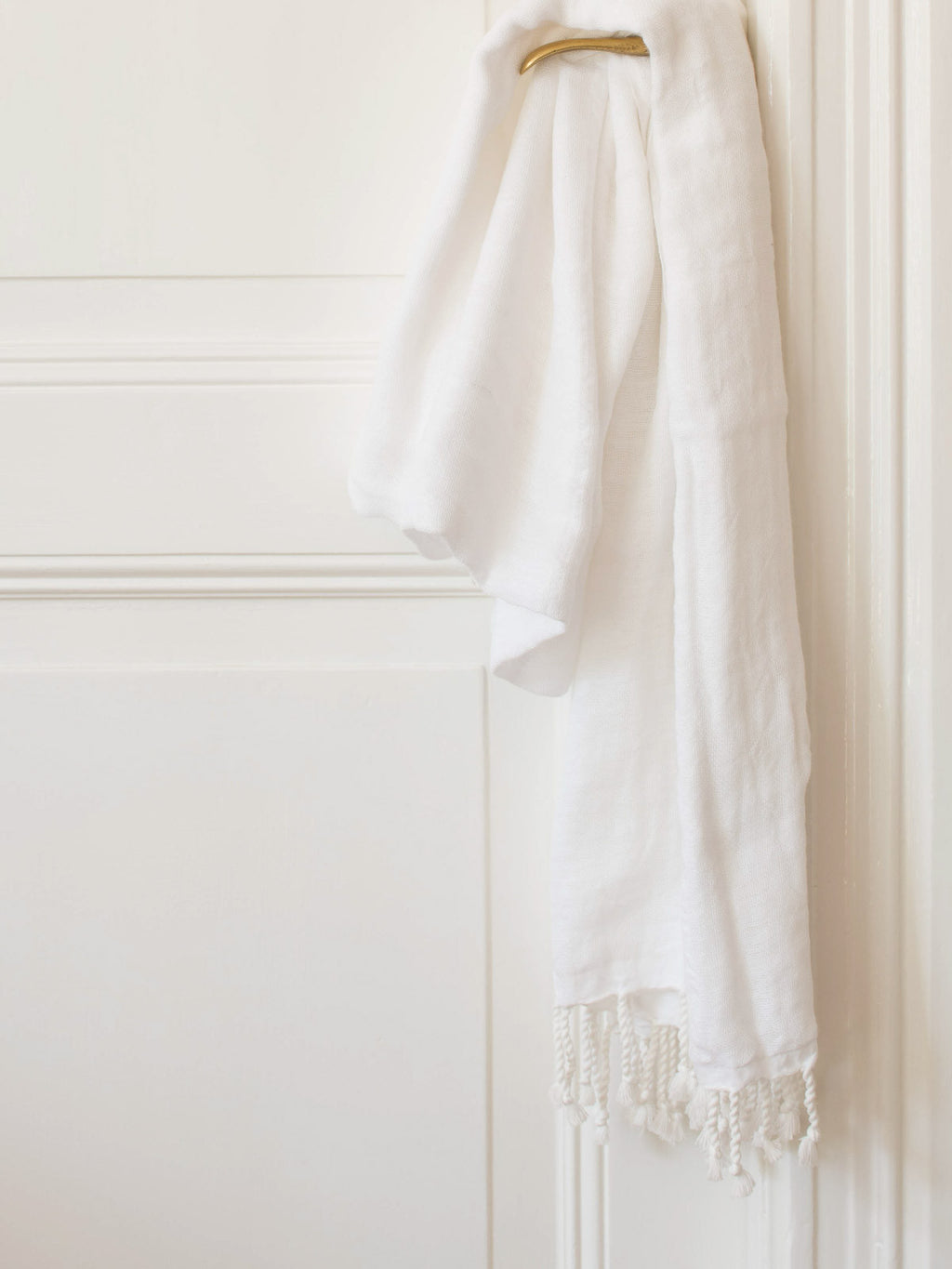 White towel with white fringes draped over a white door.
