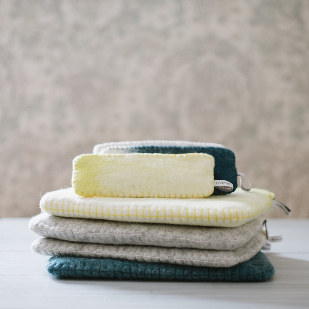 A collection of soft wool pencil cases in grey, green, and yellow, stacked together with a zippered green case on top.