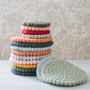 Stacked round wool trivets in various colors, designed to be used as pot holders on a table.