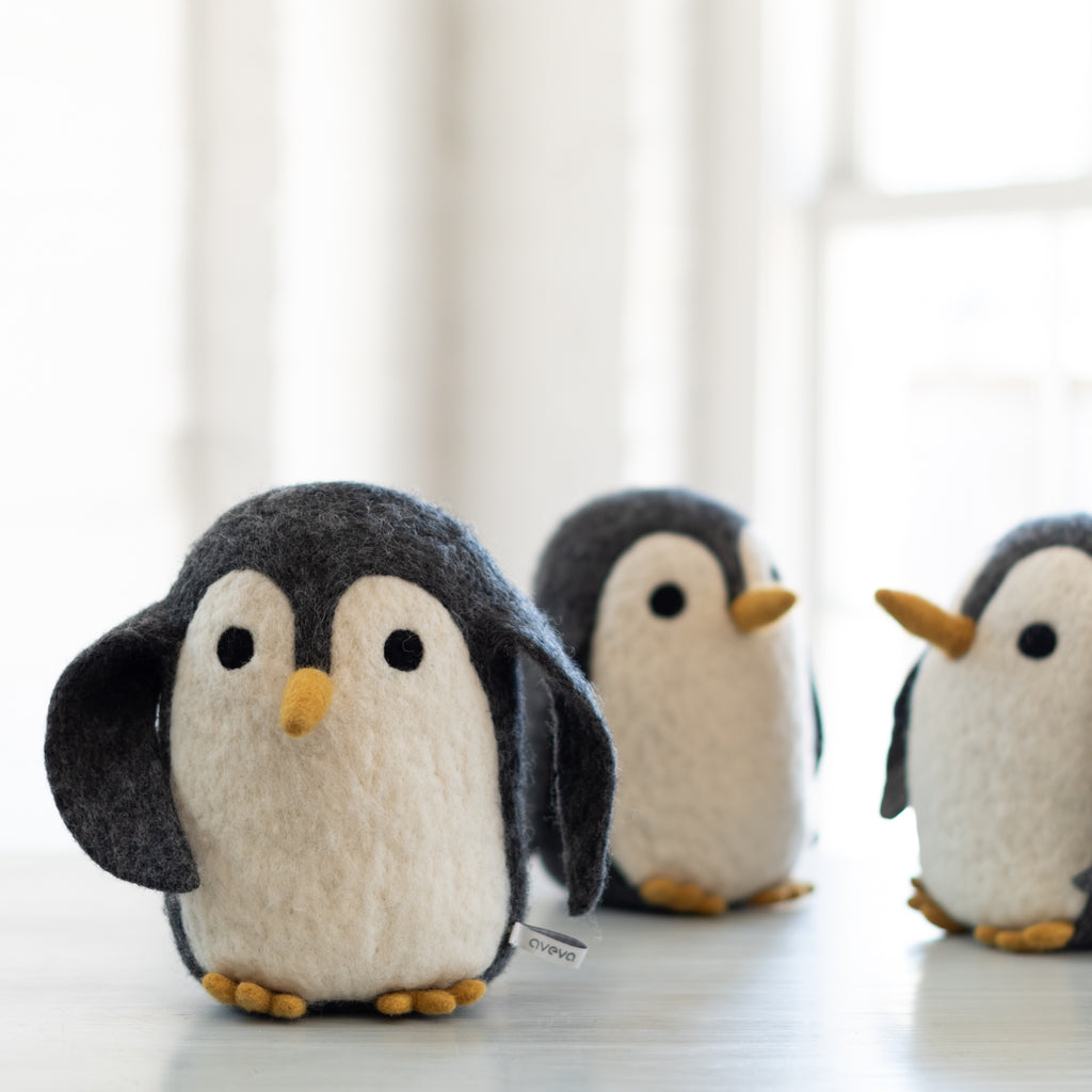 Three plush toy penguins placed on a surface, each with a pair of eyes, a beak, and a tuft of hair.